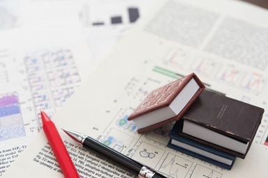 統計グラフやノートが机に並ぶ写真。研究データを解析し論文を執筆している場面のイメージ